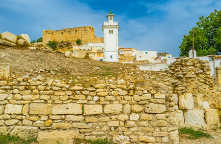 The ancient walls of the Roman baths with the white minaret and medieval Kasbah on the background, El Kef, Tunisia.の写真素材