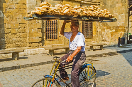 CAIRO, EGYPT - OCTOBER 12, 2014: The elderly man delivers the flatbread, riding on the cycle with...