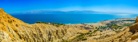 The mountains of Judean desert overlook the Dead Sea and its coastline with green palms of the local...