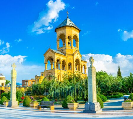The high stone bell tower of Sameba (Trinity) Cathedral, surrounded by lush green garden, Tbilisi,...