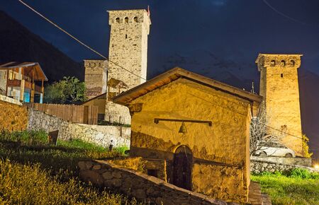 The tiny chapel on the old cemetery with the brightly illuminated Svan towers on the background, Mestia, Upper Svaneti, Georgia.の写真素材