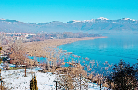 The picturesque Orestiada Lake, surrounded by yellow reeds and snowy mountains, Kastoria, Greece.の写真素材
