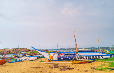 HIKKADUWA, SRI LANKA - DECEMBER 5, 2016: The walk among the colorful fishing boats on the beach with the fishermen unweigh their catch on background, on December 5 in Hikkaduwa.のeditorial素材