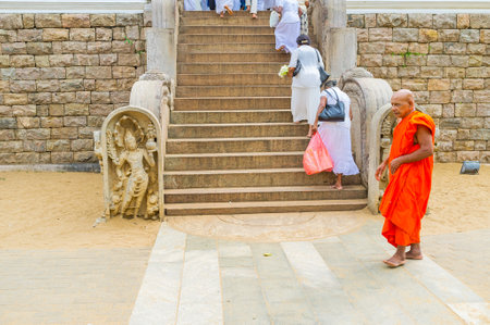 ANURADHAPURA, SRI LANKA - NOVEMBER 26, 2016: The Buddhist monk in bright orange robe at the staircase to Bodhi Tree Temple, with the guardstone of Naga-Raja from the left, on November 26 in Anuradhapura.のeditorial素材
