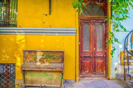 The vintage piano with the crumbling paint, stands next to the house entrance, Tbilisi, Georgia.の写真素材