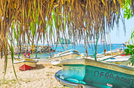 MIDIGAMA, SRI LANKA - DECEMBER 3, 2016: The view on the beach and old fishing boats through the palms' branches, on December 3 in Midigama.のeditorial素材