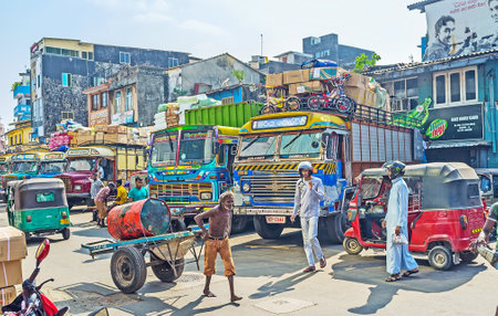 COLOMBO, SRI LANKA - DECEMBER 6, 2016: The aged porter with barrel on trolley walks along the colorful trucks, parked in Pettah, on December 6 in Colombo.のeditorial素材