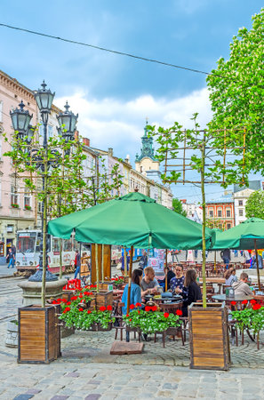 LVOV, UKRAINE - MAY 16, 2017: The cozy outdoor cafe in Market Square (Ploshcha Rynok) decorated with flowers and plants, surrounded by vintage streetlight and located next to the monument of Greek goddess Diana, on May 16 in Lvov.のeditorial素材