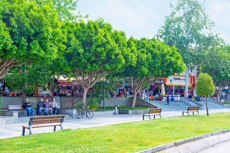 ANTALYA, TURKEY - MAY 6, 2017: The small park at the noisy Republic Avenue (Cumhuriyet Cadessi) with green trees, benches and market stalls on background, on May 6 in Antalya.のeditorial素材