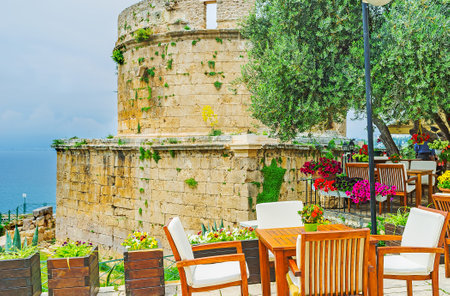 The wooden tables and chairs of the cozy outdoor restaurant next to the Hidirlik Tower - the antique landmark, preserved since the times of Romans, Kaleici, Antalya, Turkey.のeditorial素材