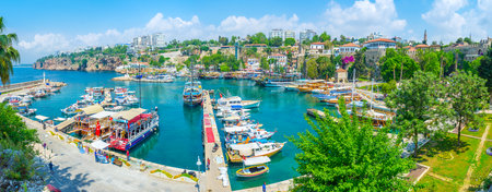 ANTALYA, TURKEY - MAY 6, 2017: Panorama of old marina with numerous yachts and boats, greenery around the embankment, ruins of the city walls, high cliffs, hotels, cafes and bars, on May 6 in Antalya.のeditorial素材