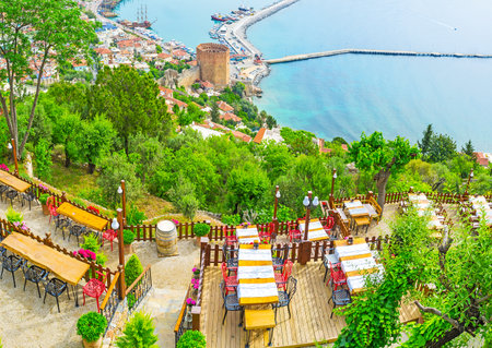 The summer terrace of the restaurant and the old Alanya on background - the Red Tower and old port are seen behind the lush fruit gardens on the Castle Hill, Turkey.のeditorial素材