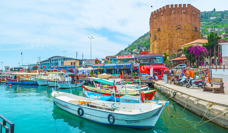 ALANYA, TURKEY - MAY 9, 2017: Panorama of old port with fishing boats, tourist restaurants and the Red Tower of arsenal on the background, on May 9 in Alanya.のeditorial素材