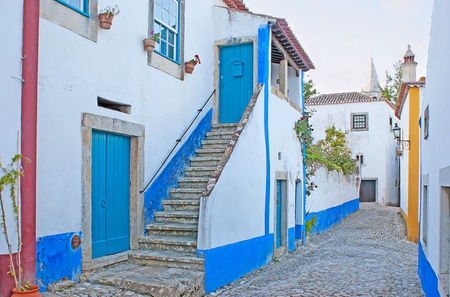 The white houses of Obidos are decorated with bright blue or yellow stripes according to the old beliefs, Portugal.の写真素材