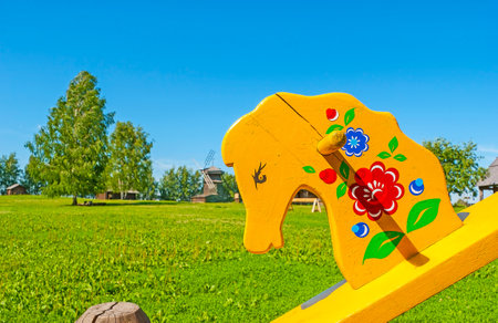 The bright painted horse seesaw with old wooden windmill on the background, Suzdal museum of wooden architecture, Russia.のeditorial素材