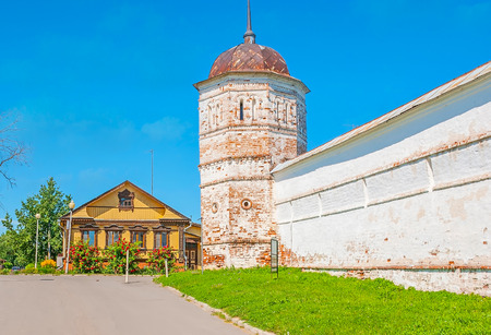 The massive brick wall and old tower of the Intercession Monastery, neighboring with traditional wooden houses, Suzdal, Russia.の写真素材