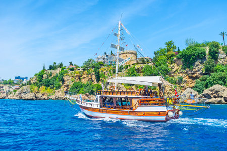 ANTALYA, TURKEY - MAY 12, 2017: The tourist yacht sails along the rocky coast of resort, people enjoy the beauty of nature and old Ottoman architecture, on May 12 in Antalya.のeditorial素材