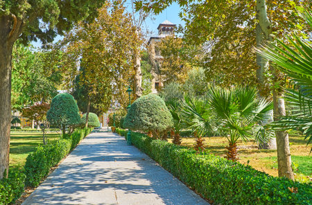 The alley among the lush greenery of Golestan garden leads to the Edifice of Sun with tall towers, Tehran, Iran.のeditorial素材