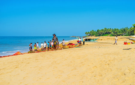 BENTOTA, SRI LANKA - DECEMBER 6, 2016: The scenic tropic beach with a group of fishermen, standing at their seine with a catch, on December 6 in Bentota.のeditorial素材