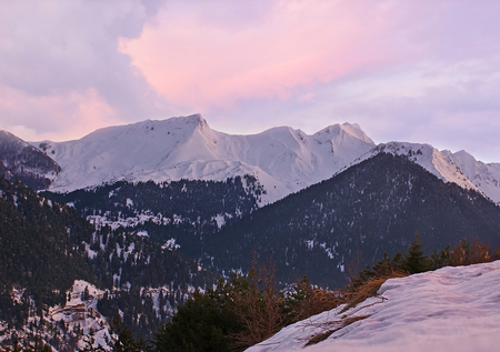 The viewpoint in Metsovo overlooks the snowbound peaks of Pindus mountains, coniferous forests on its slopes and the sunset sky, Greece.の写真素材
