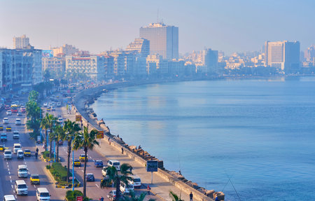 ALEXANDRIA, EGYPT - DECEMBER 17, 2017: The light morning haze over the seaside promenade - Corniche, with fast chaotic traffic and tall palm trees, on December 17 in Alexandria.のeditorial素材