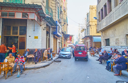 ALEXANDRIA, EGYPT - DECEMBER 17, 2017: The narrow street in Souq at Tork with numerous old tables of local teahouse, people enjoy hot black tea and shisha water pipe, on December 17 in Alexandria.のeditorial素材
