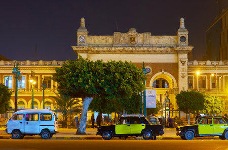 ALEXANDRIA, EGYPT - DECEMBER 17, 2017: The facade of historic building of Misr Railway Station, located in old town with black-yellow taxi cars on foreground, on December 17 in Alexandria.のeditorial素材