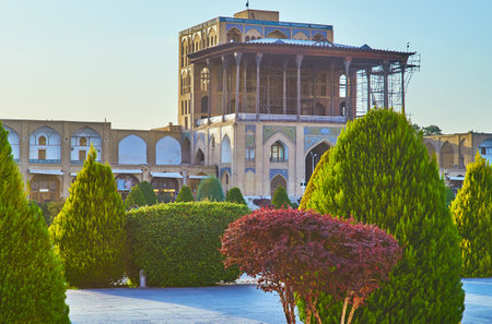 The facade of medieval Qapu palace and its large summer terrace with lush thujas and trimmed bushes of garden in Naqsh-e Jahan square on the foreground, Isfahan, Iran.のeditorial素材