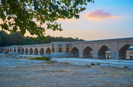 The pleasant evening walk in riverside park with a view on medieval arched Joui bridge and dried-up Zayanderud, Isfahan, Iran.の写真素材