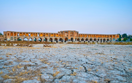 The view on scenic arched Khaju bridge, also serving as weir, with the cracked mud of dried-up Zayandeh river on the foreground, Isfahan, Iran.の写真素材