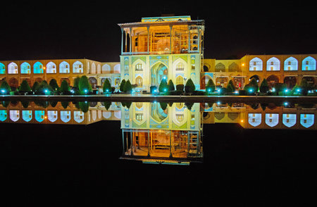 The landmarks of Naqsh-e Jahan square are especially gorgeous at night - brightly illuminated Qapu palace and Grand Bazaar galleries are reflected on clear surface of the pond, Isfahan, Iran.のeditorial素材