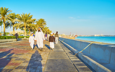 DOHA, QATAR - FEBRUARY 13, 2018: Arab family - father and sons in traditional dress walk along the Corniche promenade, on February 13 in Doha.のeditorial素材