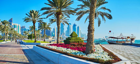 DOHA, QATAR - FEBRUARY 13, 2018: Panorama of seaside park with trimmed bushes, lush palms and colored flower beds on Corniche promenade in business Al Dafna district, West Bay, on February 13 in Doha.のeditorial素材