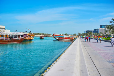 DOHA, QATAR - FEBRUARY 13, 2018: The beautiful seaside Corniche promenade with pleasure boats, moored in harbor and lush greenery along the walkway, on February 13 in Dohaのeditorial素材