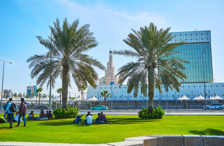 DOHA, QATAR - FEBRUARY 13, 2018: The locals enjoy the daily rest on the picnics in Corniche promenade with a view on spiral minaret of Al Fanar mosque on the background, on February 13 in Dohaのeditorial素材