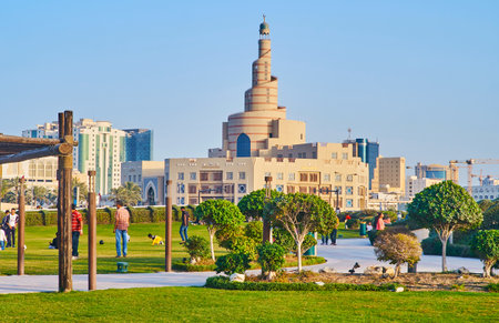 DOHA, QATAR - FEBRUARY 13, 2018: People walk and play games in Souq Waqif park with spiral minaret of Al Fanar Mosque on background, on February 13 in Doha.のeditorial素材