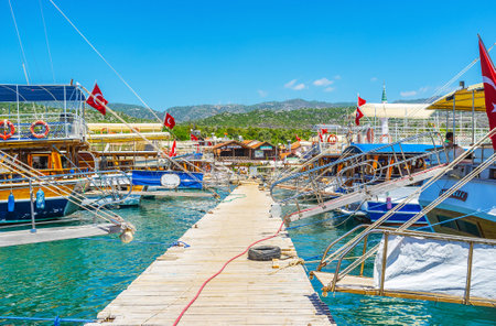 KEKOVA, TURKEY - MAY 10, 2017: The wooden pier with rows of yachts and pleasure boats on both sides and small village cottages on the background, on May 10 in Kekova.のeditorial素材
