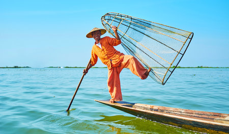 INLE LAKE, MYANMAR - FEBRUARY 18, 2018: Traditional Burmese fisherman poses while standing on one leg and holding the conical net in his kayak on Inle Lake, on February 18 in Inle lake.のeditorial素材