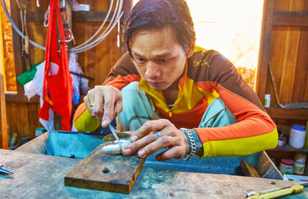 INPAWKHON, MYANMAR - FEBRUARY 18, 2018: The Burmese silversmith polishes the bracelet in jewelry...