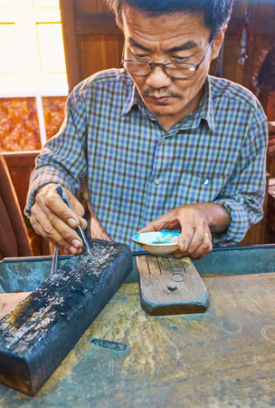INLE LAKE, MYANMAR - FEBRUARY 18, 2018: The silversmith produces the jewelries, heating up earrings blank with burner in workshop-store on Inle lake, on February 18 in Inle lake.のeditorial素材