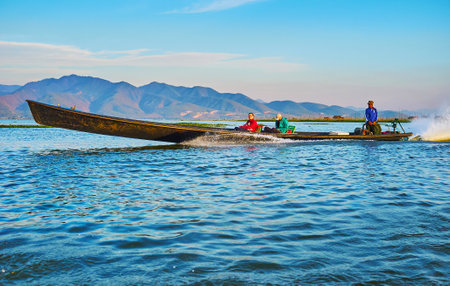 INTHA, MYANMAR - FEBRUARY 18, 2018: The smiling tourists in fast floating kayak on Inle Lake with mountain range on the background, on February 18 in Intha.のeditorial素材