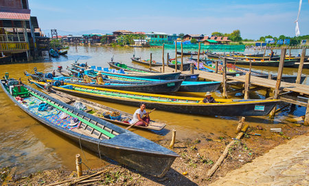 YWAMA, MYANMAR - FEBRUARY 18, 2018: The wharf with moored kayaks and the boat of the food celler, offering traditional Burmese snacks and fresh fruits to pilgrims and tourists, coming from the Buddhist site, on February 18 in Ywama.のeditorial素材