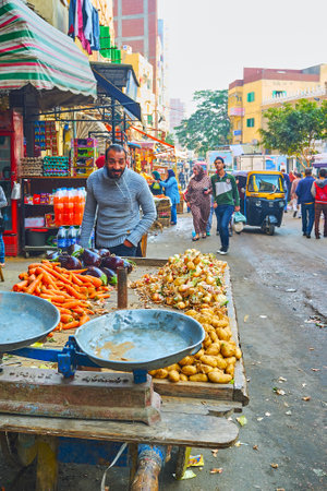 ALEXANDRIA, EGYPT - DECEMBER 18, 2017: The souq (market) street of Karmouz with balance skales on the old cart with vegetables and smiling vendor on background, on December 18 in Alexandria.のeditorial素材