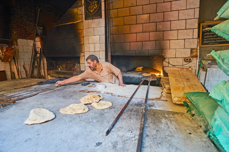 ALEXANDRIA, EGYPT - DECEMBER 18, 2017: The baker and tasty flatbread, just from the oven on the table in small bakery-store of Karmouz district, on December 18 in Alexandria.のeditorial素材