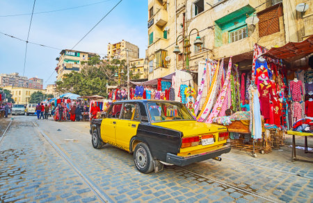 ALEXANDRIA, EGYPT - DECEMBER 18, 2017: The old taxi rides along the busy Karmouz avenue, with row of clothing stores on background, on December 18 in Alexandria.のeditorial素材