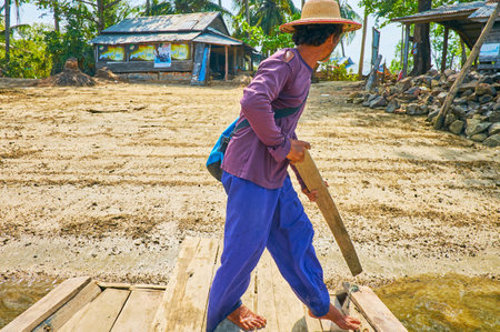THAZIN, MYANMAR - FEBRUARY 28, 2018: The raftman uses the plank to push off the river's bank with a view on village houses on background, on February 28 in Thazinのeditorial素材