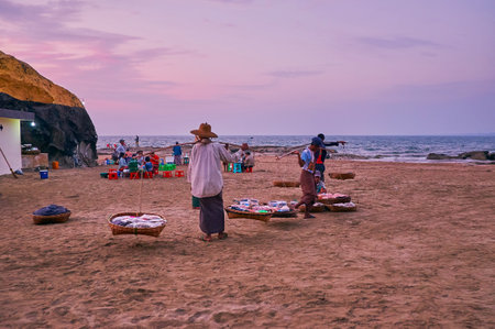 CHAUNG THA, MYANMAR - FEBRUARY 28, 2018: The street food vendors with baskets on the yokes offer their goods at Kyauk Pa Hto Pagoda on sunset, on February 28 in Chaung Tha.のeditorial素材