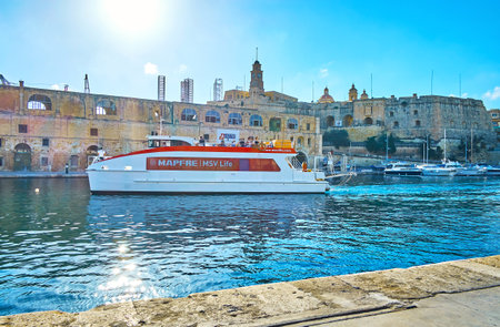 BIRGU, MALTA - JUNE 17, 2018: The modern ferry with tourists is arriving to the terminal of Birgu,  maneuvering in narrow Vittoriosa marina with a view on St Michael's bastion of Senglea (L-Isla) fortress, on June 17 in Birgu.のeditorial素材