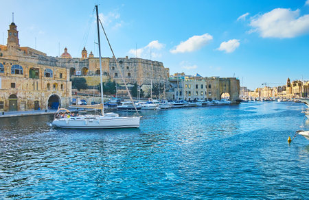 BIRGU, MALTA - JUNE 17, 2018: Scenic sail yacht floats in marina of Vittoriosa with a view on medieval St Michael's and Sheer bastions of Senglea (L-Isla) fortress on background, on June 17 in Birgu.のeditorial素材