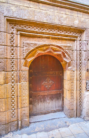 The medieval carved stone doorframe with metal cross on the door of the old edifice, in Coptic district of Cairo, Egyptのeditorial素材